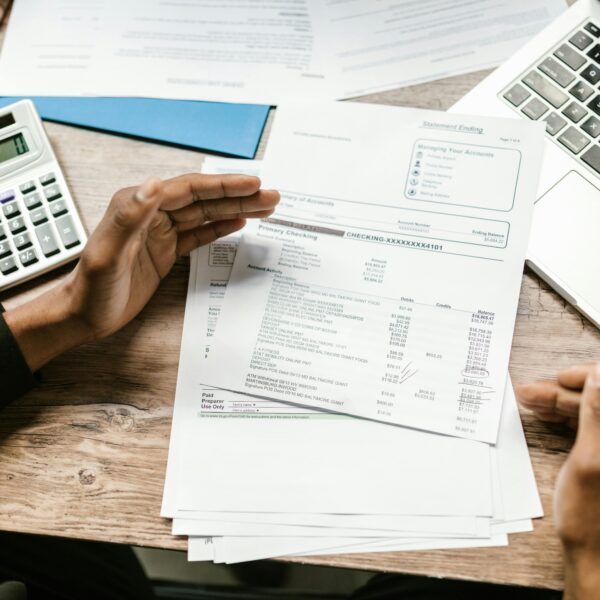 Hands holding financial documents with calculator and laptop on office desk, business analysis scene.